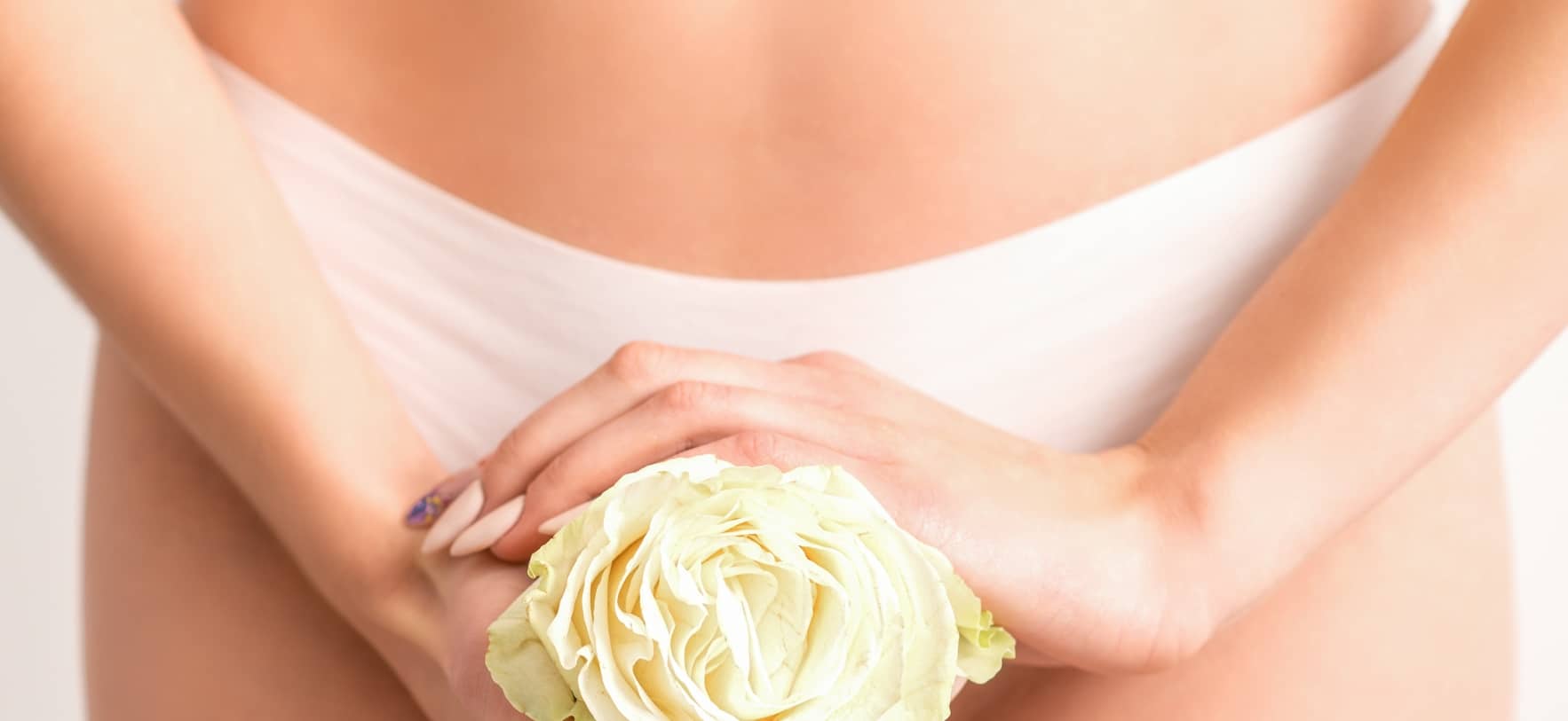 Eine Frau hält eine zarte Blume in ihren Händen. Sie bedeckt damit Ihre Bikinizone als Symbolbild für eine Intimkorrektur.